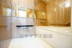 木目調パネルが上質な雰囲気を演出するバスルームは、一日の疲れをゆったり癒せるくつろぎ空間。広々とした浴槽に加え、使いやすい収納棚や手すりを備え、安全性と快適性の両方に配慮された設計です。